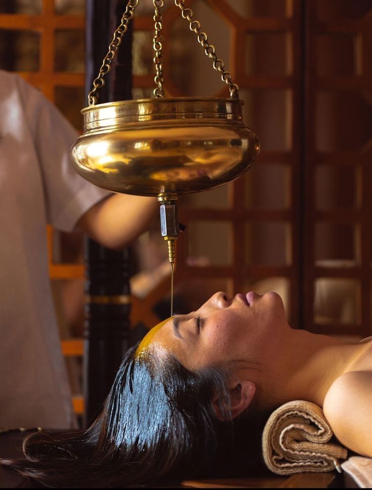 Shirodhara treatment with medicated oil streaming from brass vessel over forehead